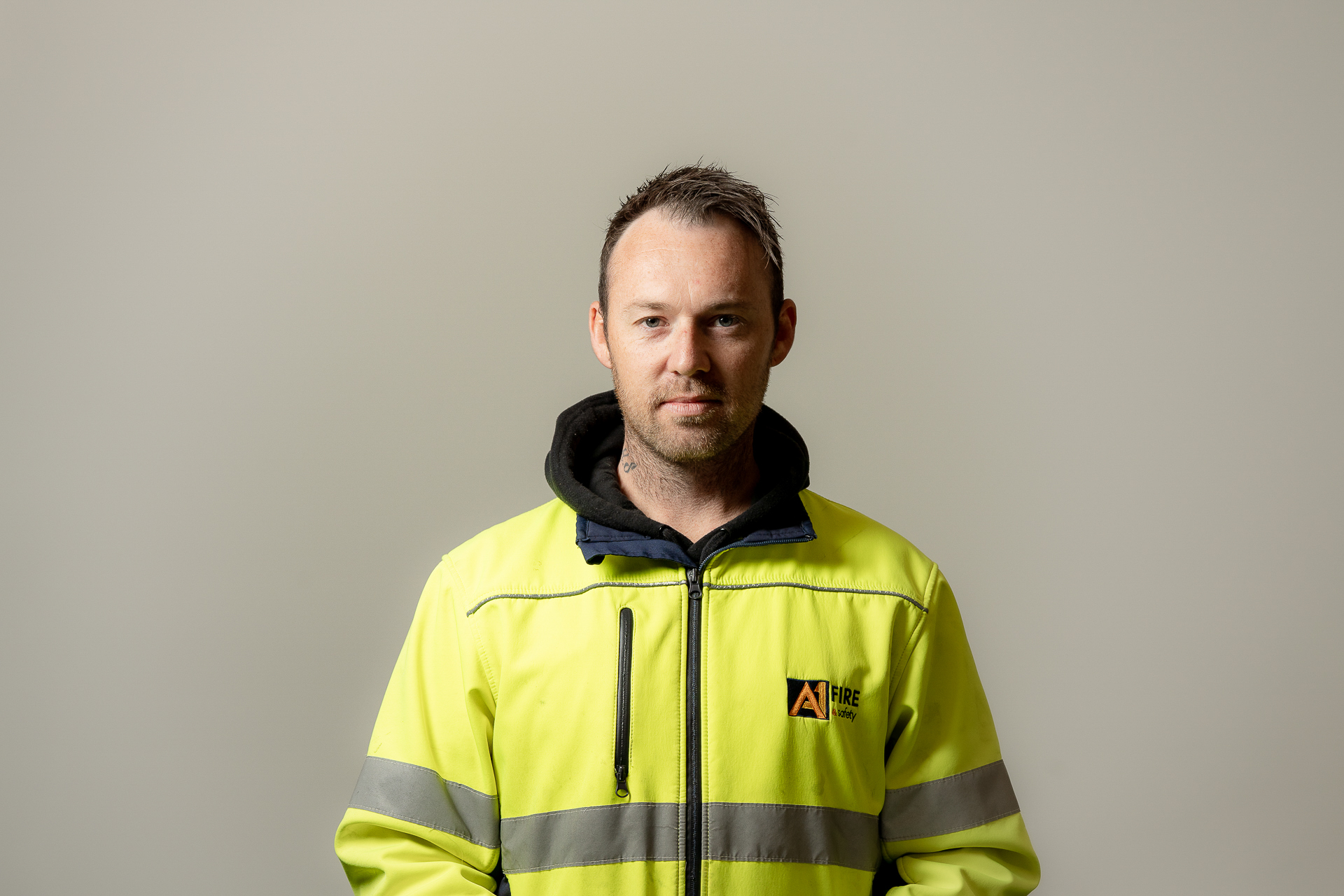 A person in a high-visibility yellow jacket stands facing forward against a plain background. The demeanor is calm and professional.