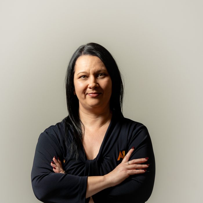Woman with long black hair and a black top stands confidently against a neutral background, arms crossed, conveying a sense of strength and self-assurance.