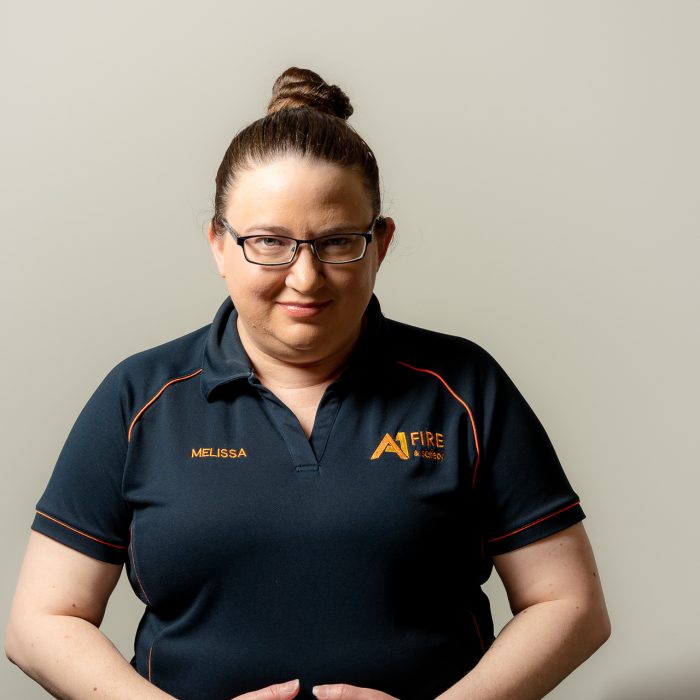 Woman with glasses and a bun wearing a navy polo shirt with orange stitching, standing against a neutral background. Friendly expression.